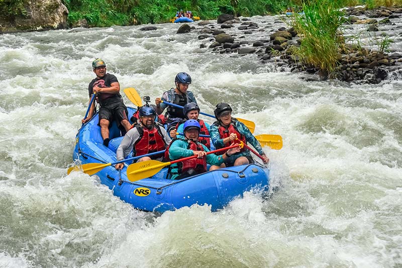 A group of people enjoying a rafting adventure on a river in Costa Rica, with white water and lush greenery in the background.